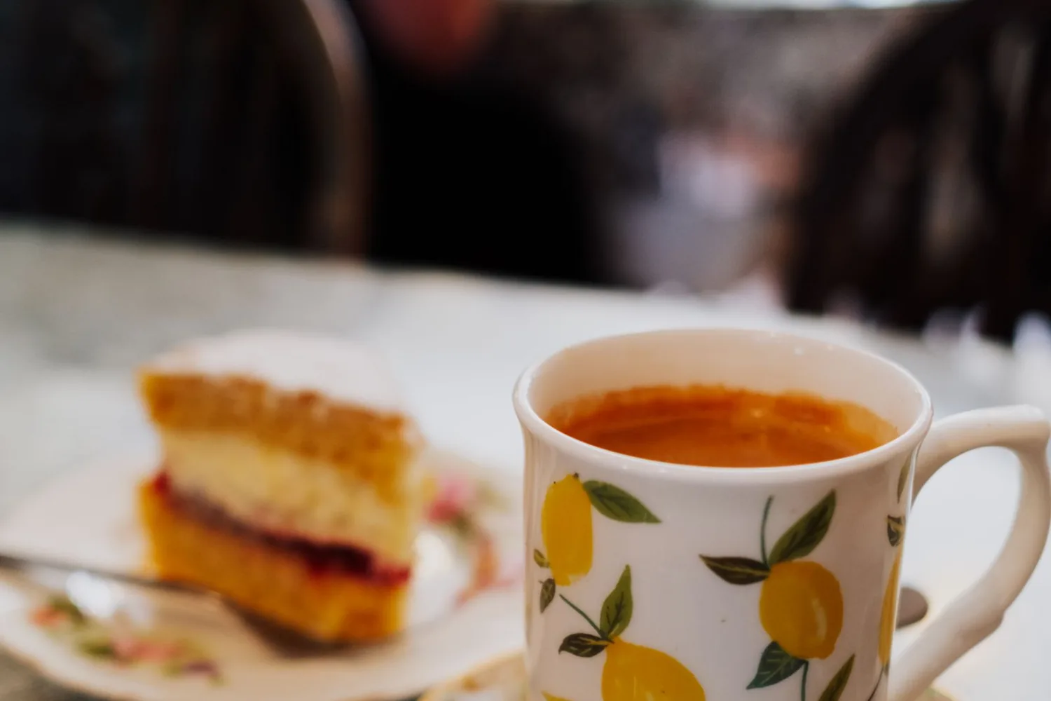 A slice of Victoria sponge with jam beside a cup of tea