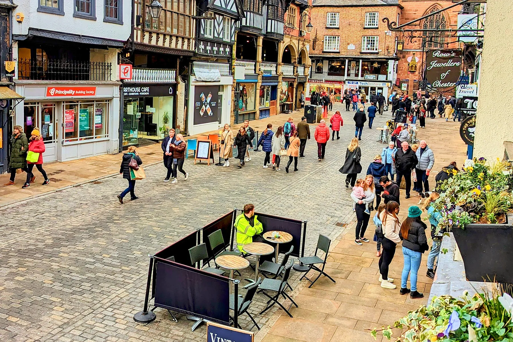 Café tables on Bridge Street below the black and white Rows, with St Peter's Church at the Cross