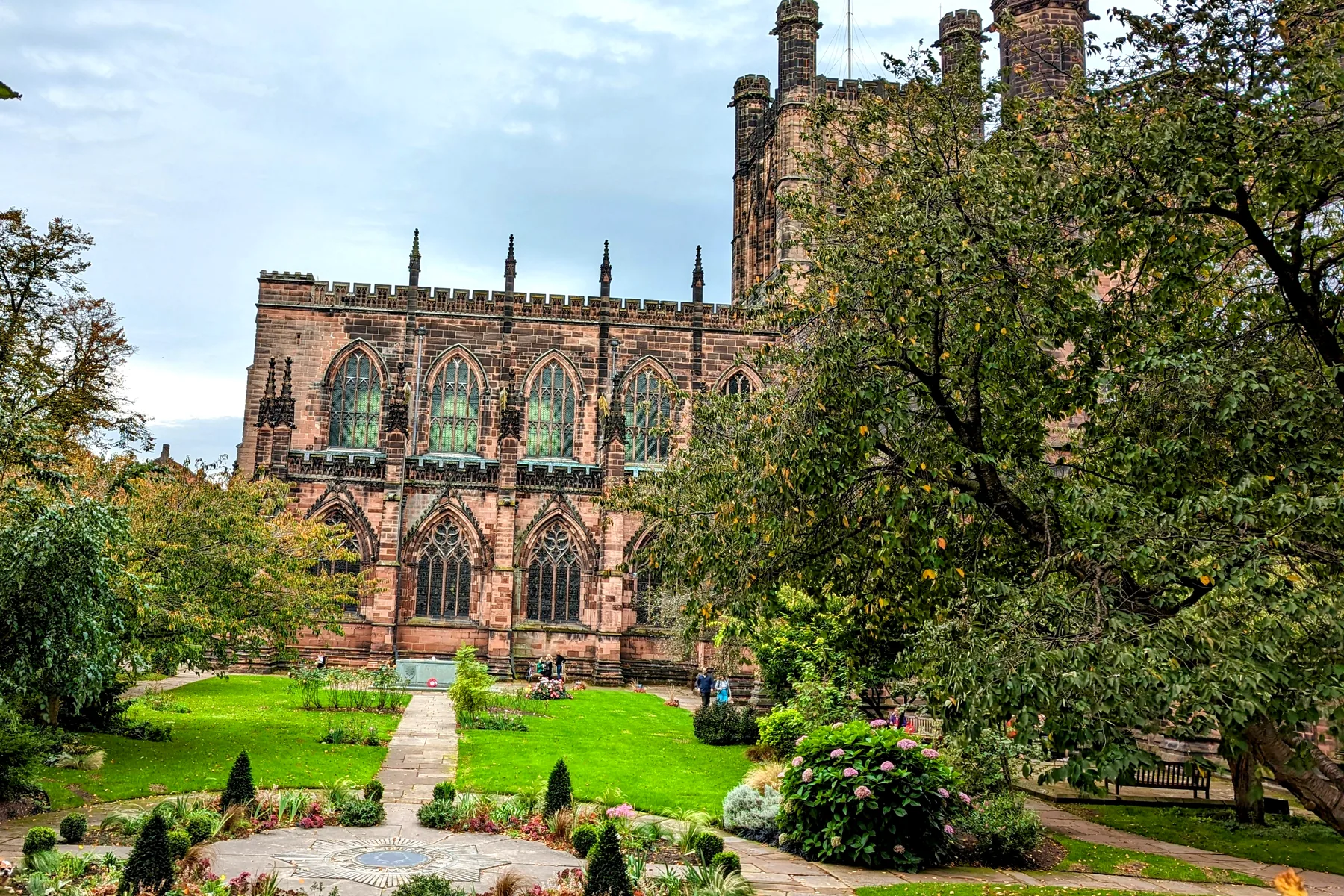 Chester Cathedral's red sandstone above its garden, with autumn leaves on the lawn