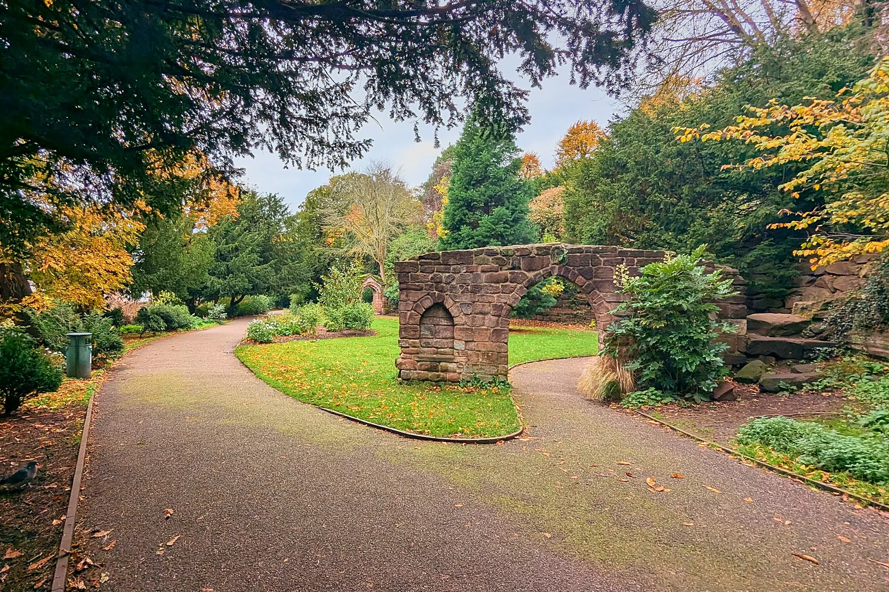 A winding path through Grosvenor Park in autumn, past an old stone arch among the trees