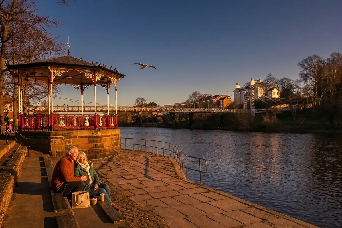 The Groves bandstand beside the River Dee at golden hour, with a couple resting on the steps