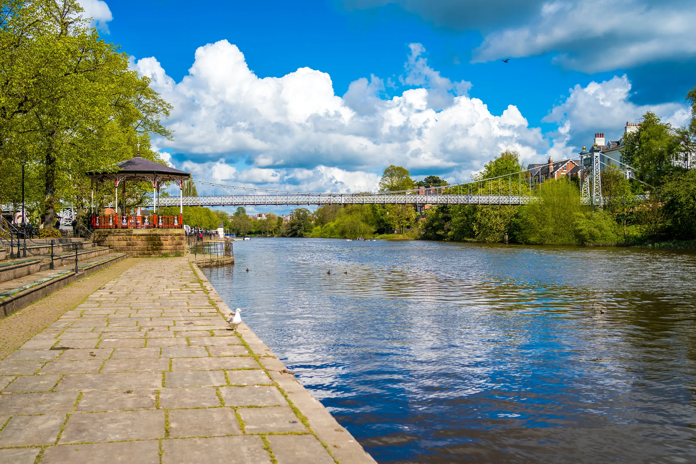 The Groves promenade beside the River Dee in summer, with the bandstand and the suspension bridge beyond