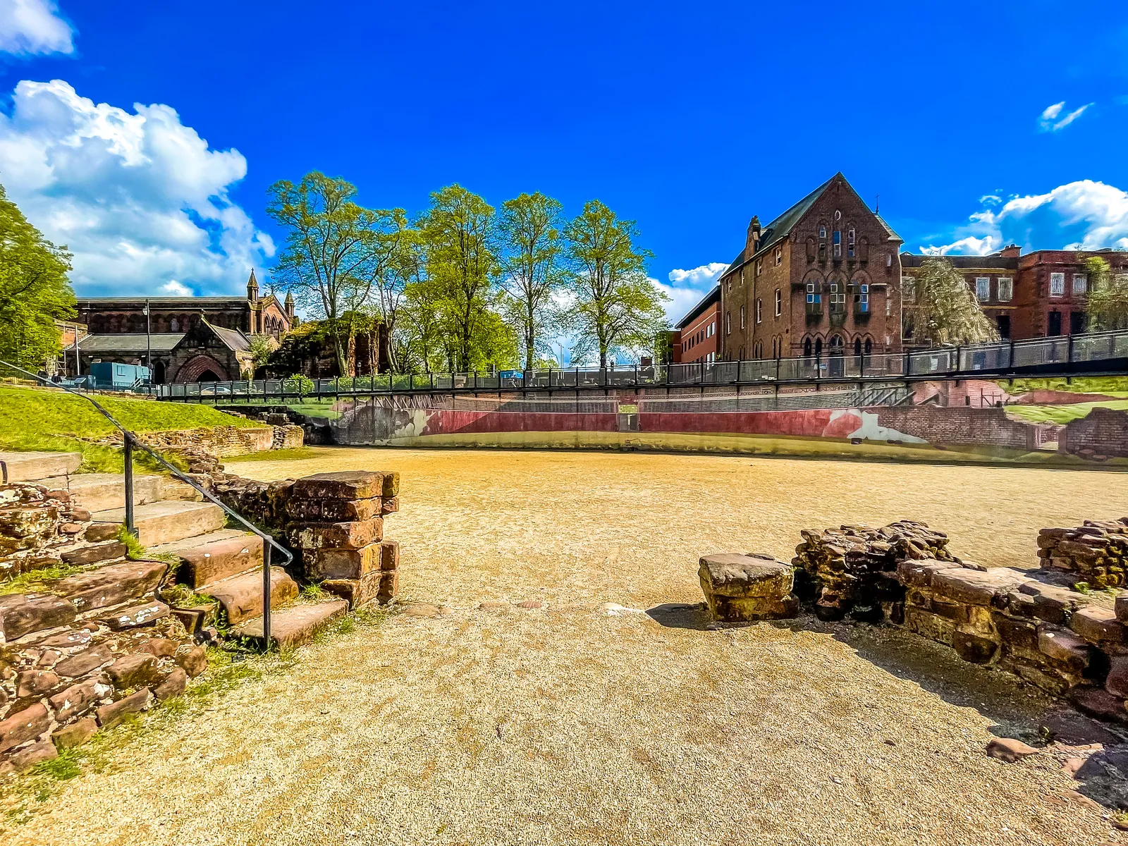 The sandy arena of Chester's Roman Amphitheatre with its low stone walls on a sunny day