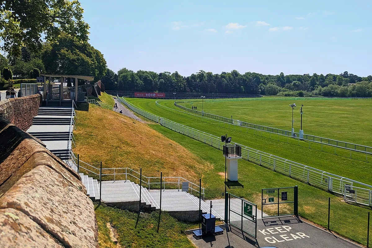 The green racecourse of the Roodee seen from the city walls, with white rails and steps down from the wall