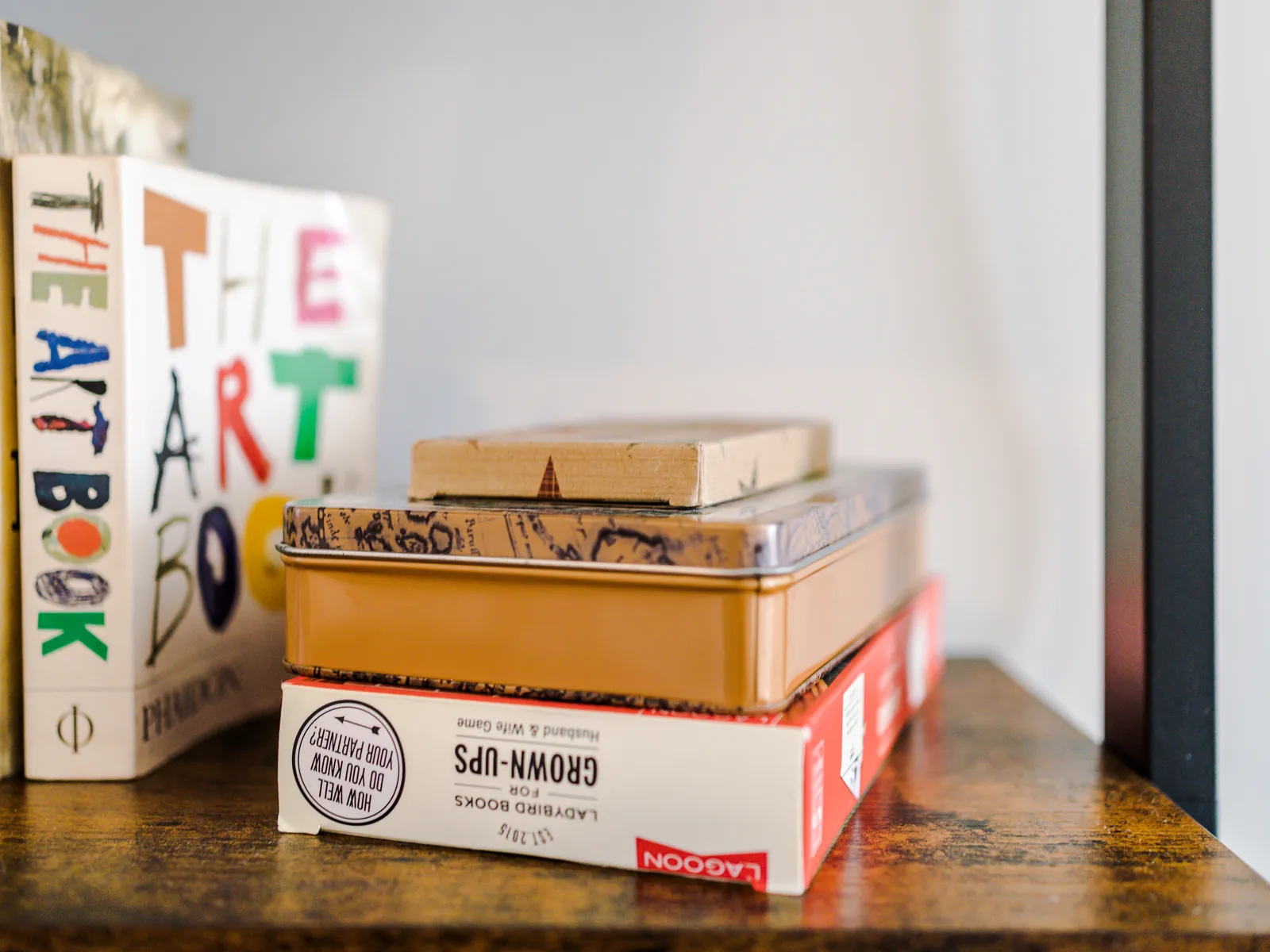 Games in tins and boxes stacked on a wooden shelf beside books
