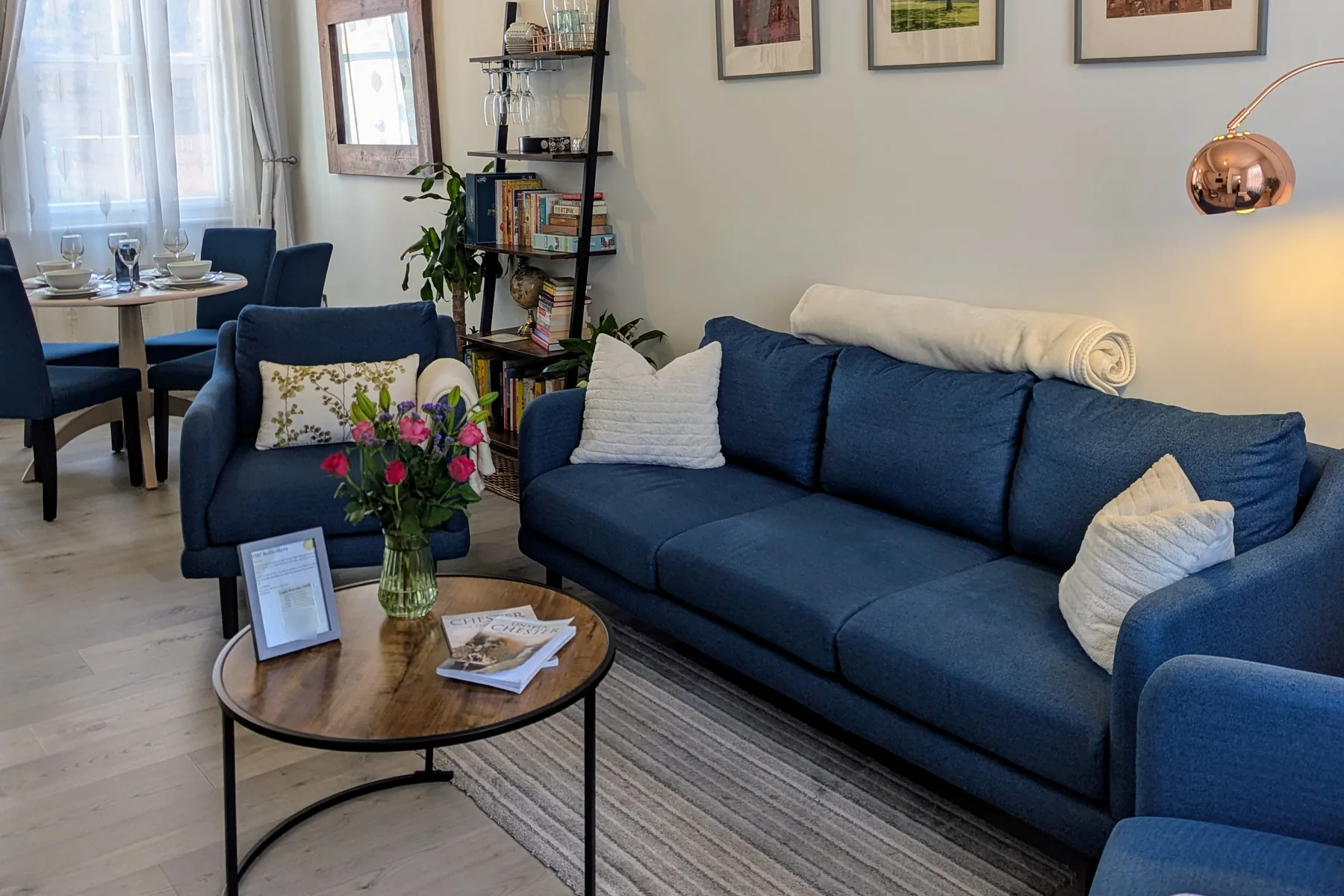 The living room with blue sofas, fresh flowers and the copper floor lamp glowing