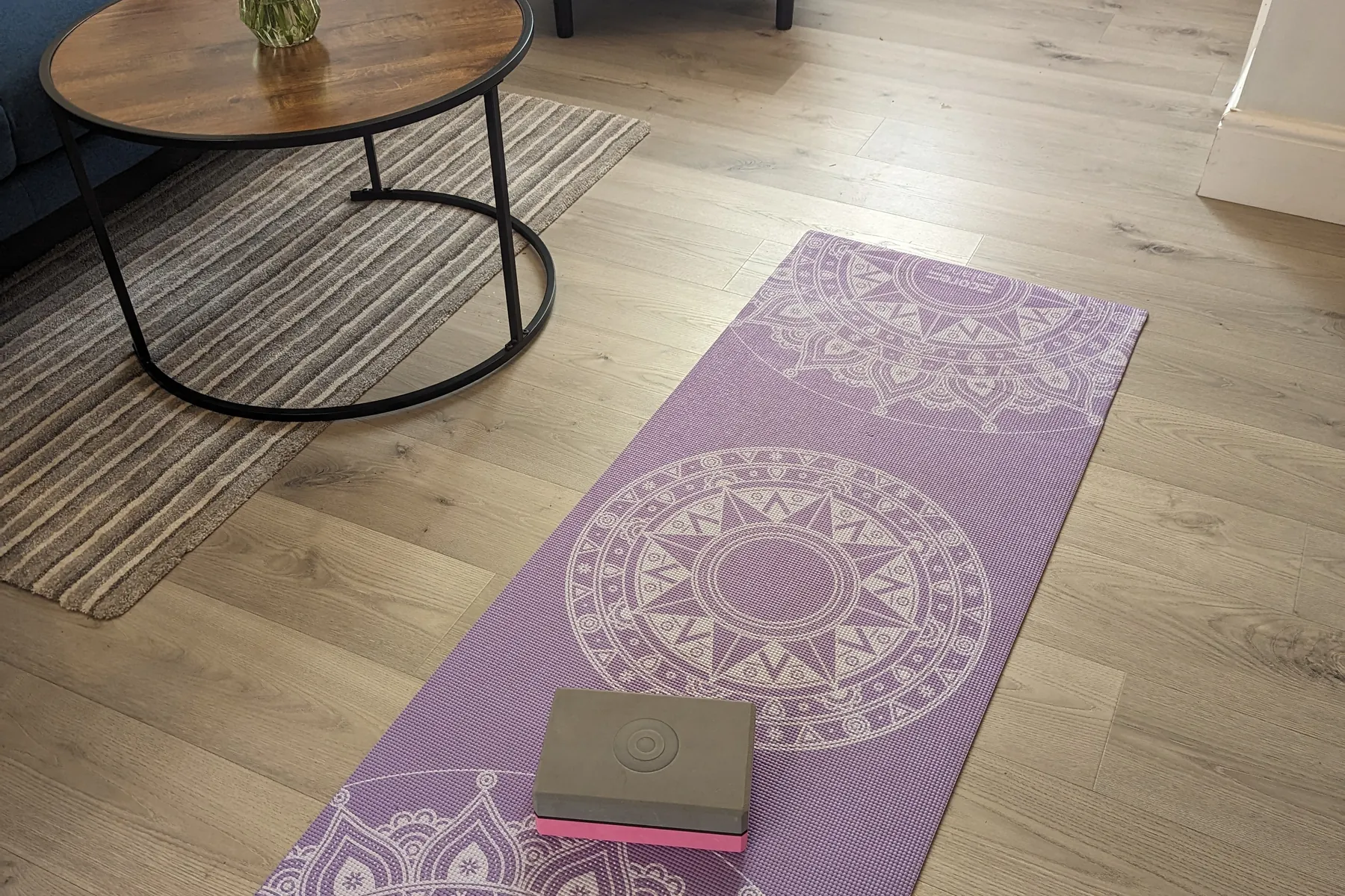 A purple yoga mat and block on the living room floor beside the round coffee table