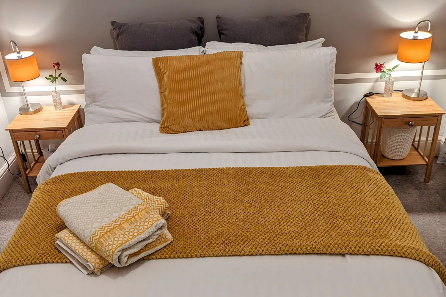 The king bed in the main bedroom with a mustard throw and both bedside lamps on