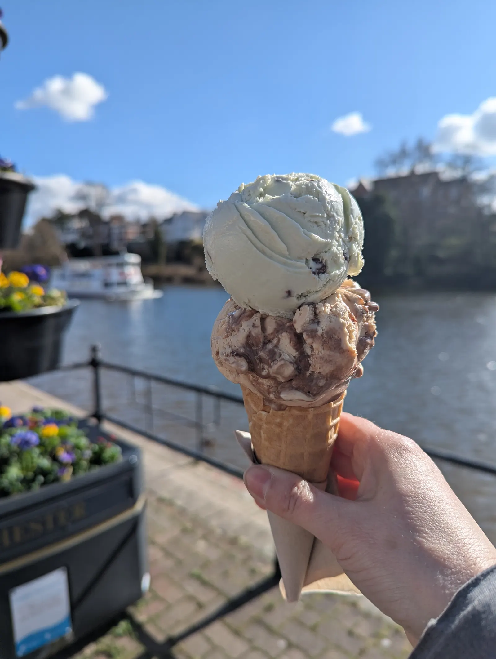 Ice cream cone held up beside the River Dee on a sunny day