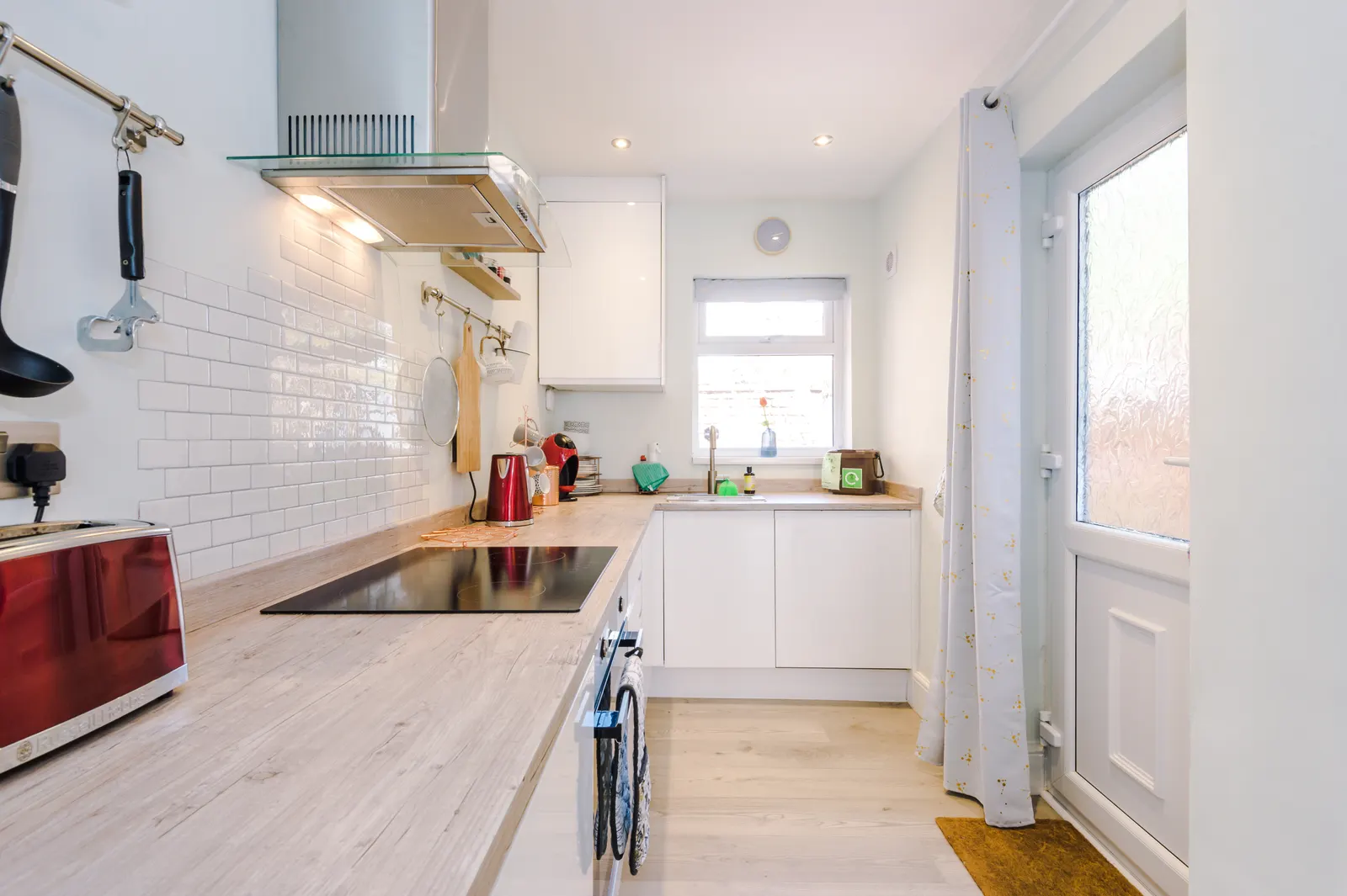 Full-length white kitchen with wooden worktops, oven and window