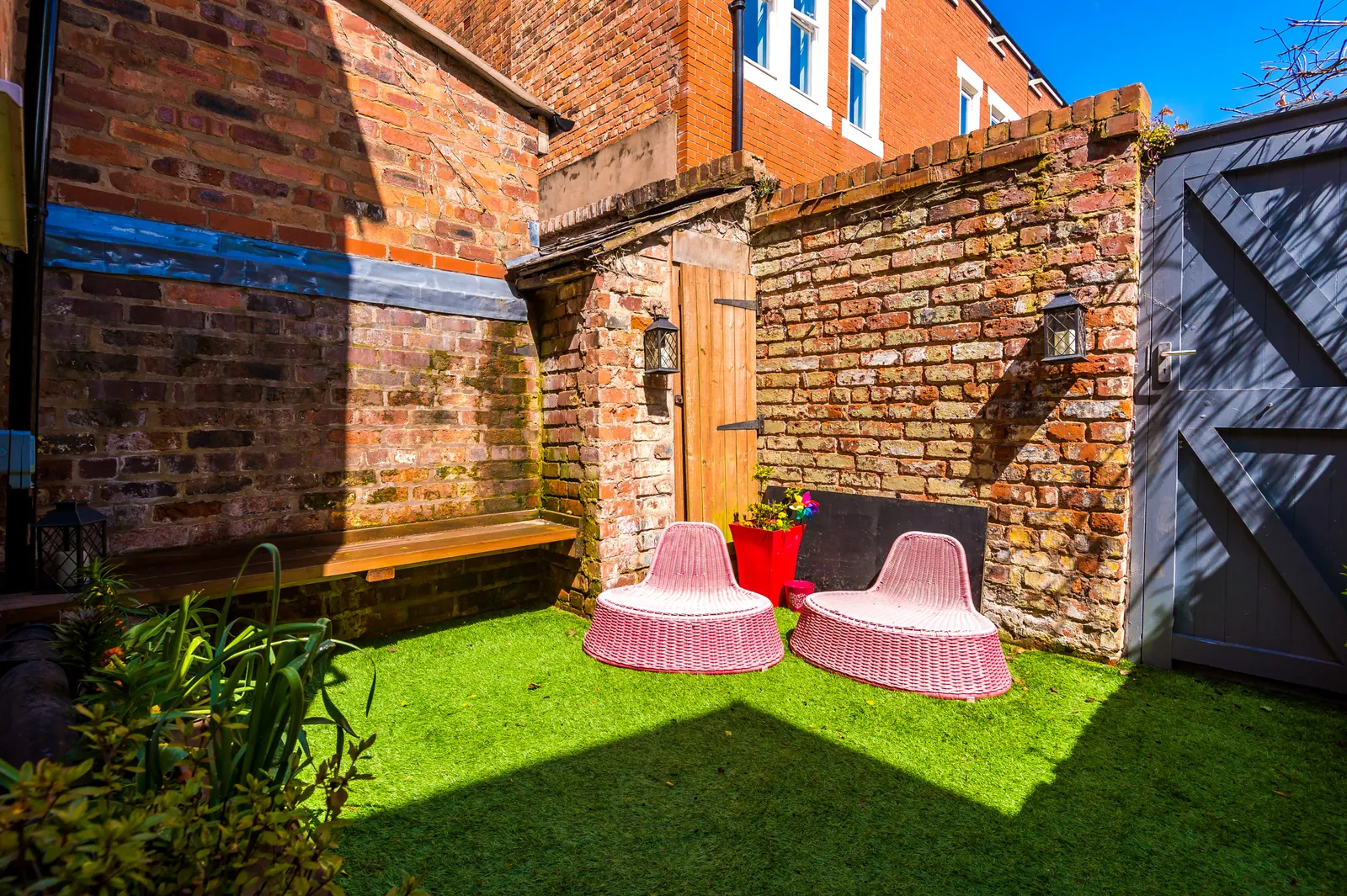 Private walled courtyard garden with artificial lawn and pink chairs in sunshine