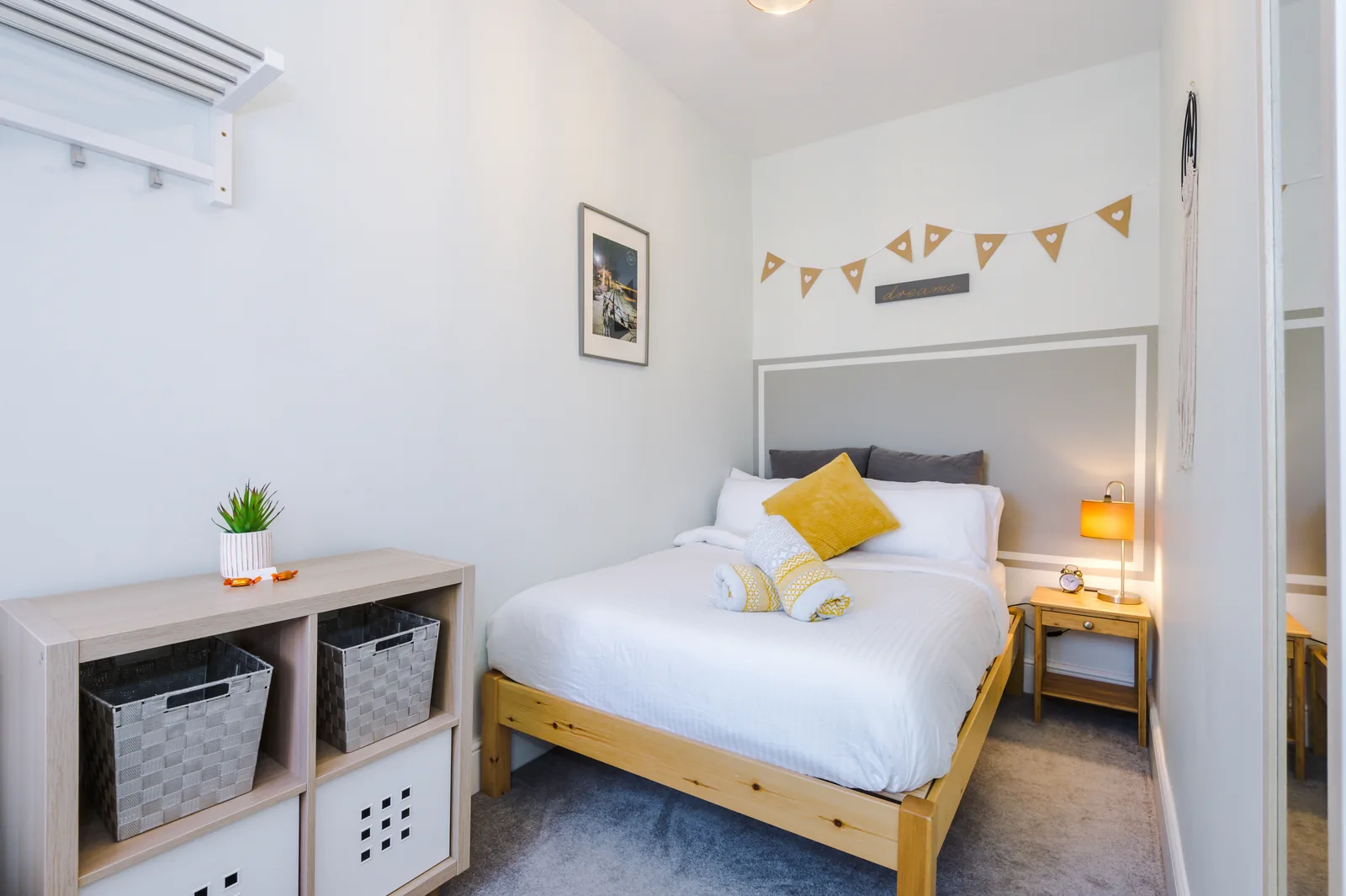 The second bedroom seen end to end, with a double bed, open storage and a bedside lamp