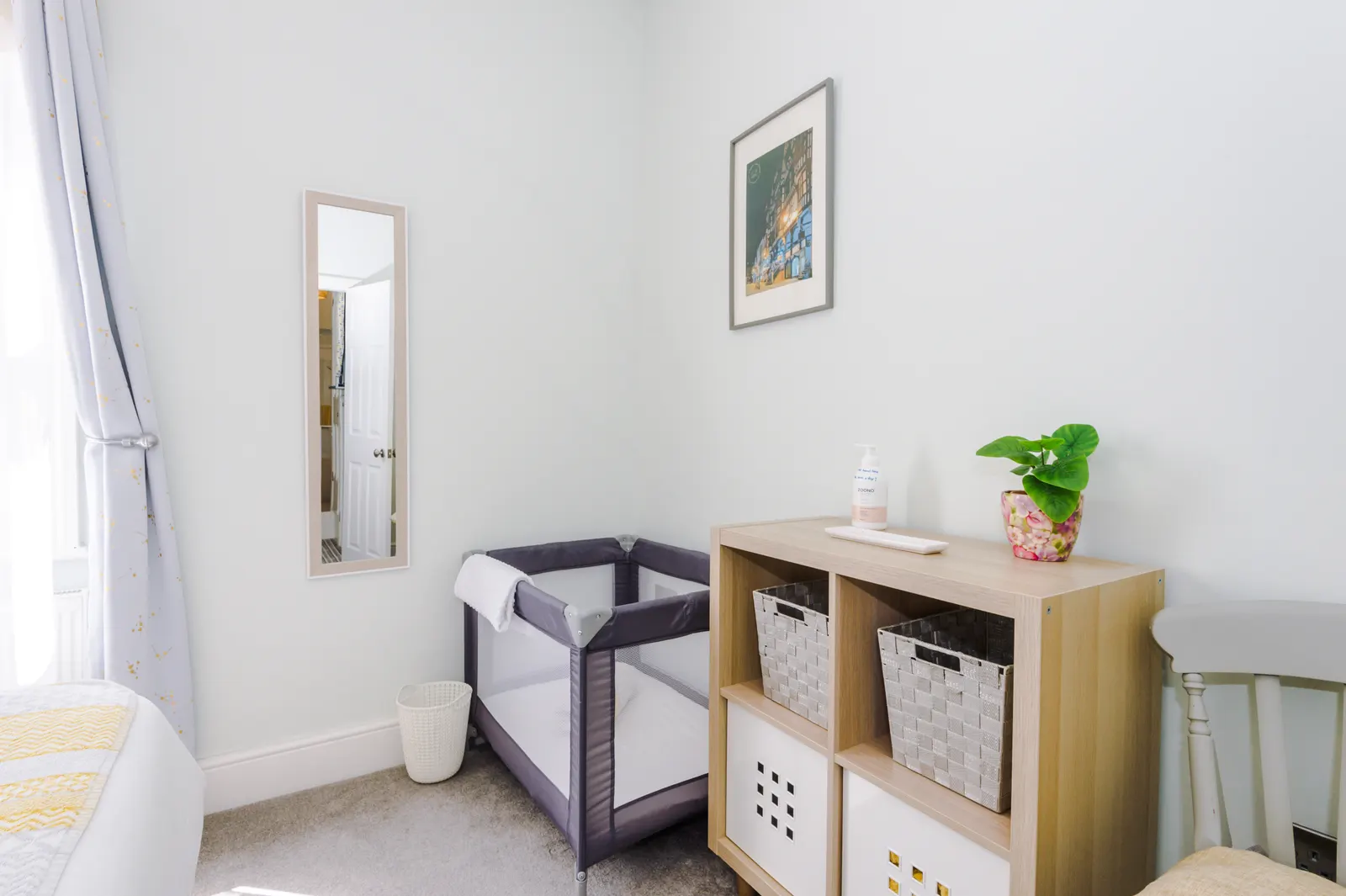 Travel cot set up beside storage shelves in the bedroom